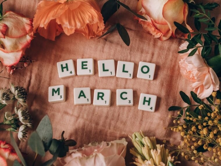 Flowers surrounding scrabble tiles that say "Hello March"
