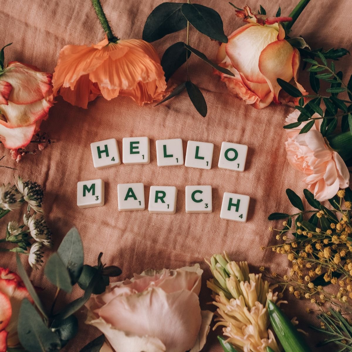 Flowers surrounding scrabble tiles that say "Hello March"